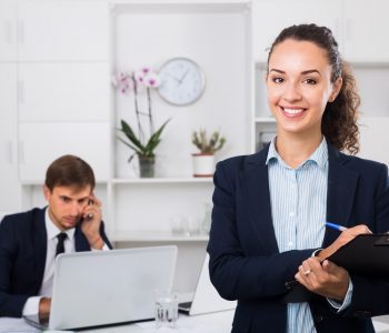 attractive young woman manager holding cardboard and smiling in office