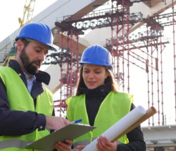 Two people male engineer and female architect discussing construction progress near the construction frame and bridge building site, looking at blueprints and documents. Footage taken in 4K resolution in Central Europe.
